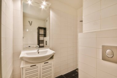 Beyaz fayansları ve siyah döşemeleri olan küçük bir banyo. Lavabo duvardaki aynanın yanında.