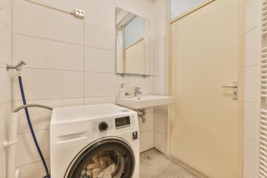 Çamaşır yıkama ve kurutma makinesi olan bir çamaşır odası banyo kapısının yanında, bir dairede ya da evde.