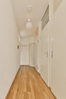 a long hallway with white walls and wood flooring on the right side, there is an open door leading to another room