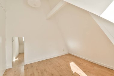 Ahşap döşemesi ve duvarlarında beyaz boya olan boş bir oda. Köşesinde bir ayna var.