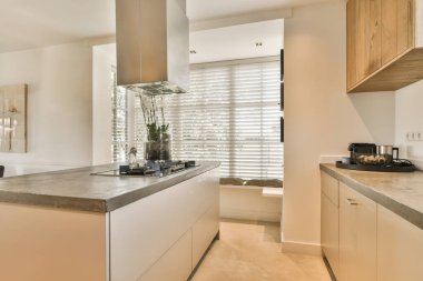 Mermer tezgahlı modern bir mutfak ve beyaz dolaplar pencereden gelen doğal ışıkla aydınlatılıyor.