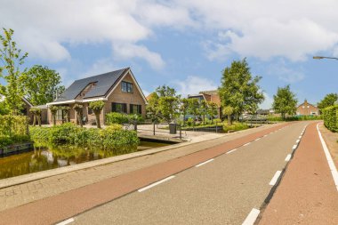 Her iki tarafında evler olan bir cadde ve fotoğrafın ortasından akan bir nehir diğer tarafından çekiliyor.