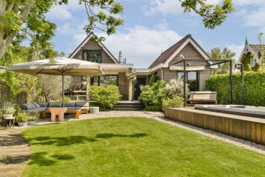 Jakuzinin üzerinde şemsiyesi olan bir arka bahçe ve evin önündeki çimlerin üzerinde şezlonglar.