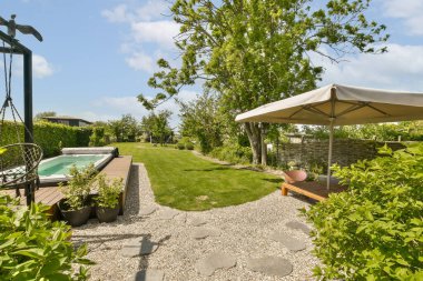 Bahçede şemsiyesi ve ön planda bitkileri olan bir alan. Güneşli bir günde küçük bir yüzme havuzu var.