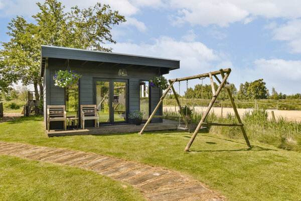 an outdoor play area with swings and swings in the grass, surrounded by blue sky and white fluffy clouds