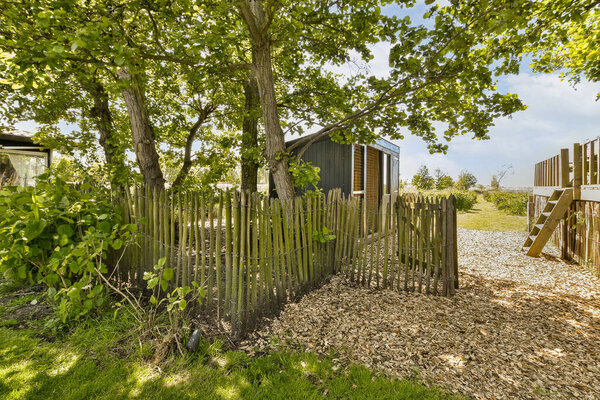 a wooden fence in the grass next to a tree and a small house on the other side of the fence