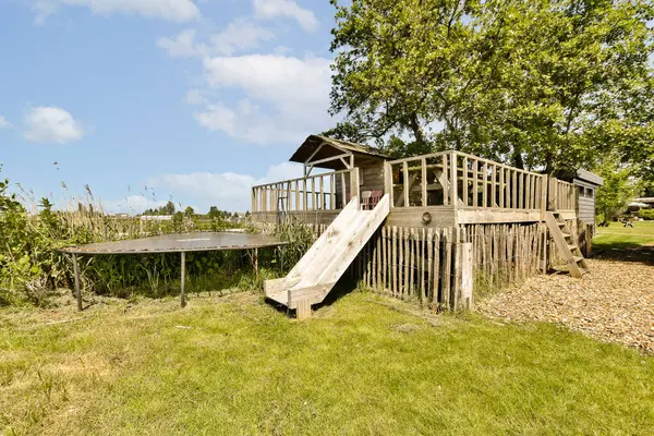 a backyard play area with a slide in the grass and a tree on the other side of the fenced area