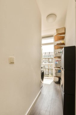 Bir dairede ahşap döşemeli ve beyaz duvarlı bir mutfak, kapıdan oturma odasına götürülmüş.