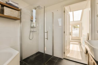 Siyah döşemeleri ve beyaz duvarları olan modern bir banyo. Köşesinde cam bir duş kabini var.