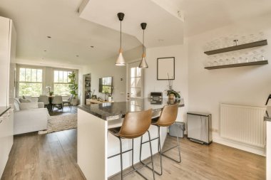 Ahşap döşemeleri, beyaz duvarları ve ahşap zemini olan bir evde mutfak ve yemek odası iyi aydınlatılmış.