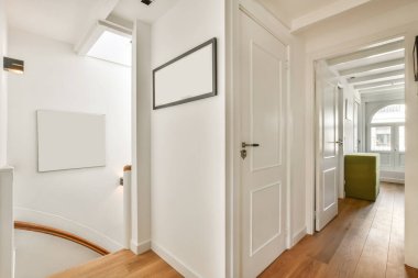 Beyaz duvarları ve ahşap döşemeleri olan bir koridor tavan penceresinden gelen doğal ışıkla aydınlanır.