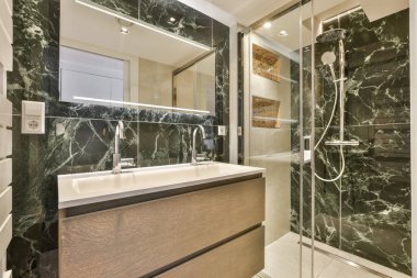 Siyah mermer duvarları ve zemini olan modern bir banyo ve sağ taraftaki duş kabininde bir yürüyüş.