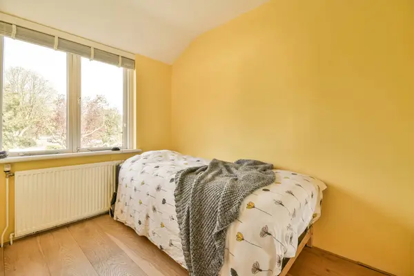 a bedroom with yellow walls and hardwood flooring, showing the light coming in through the large window panes