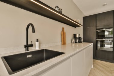 Tezgahında siyah beyaz eşyalar olan modern bir mutfak. Ortasında da bir ada lavabosu var.