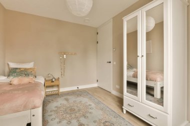 İki yataklı bir yatak odası ve yatağın önündeki duvarda bir ayna. Yatağın yanında pembe bir halı var.