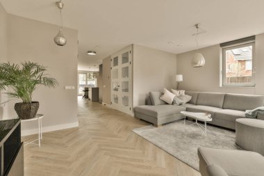 Odanın ortasında ahşap döşemeli ve beyaz duvarlı bir oturma odası gri bir kanepe, iki sandalye, bir...