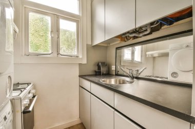 Caddeye bakan açık pencerenin önünde beyaz dolapları ve siyah tezgahları olan bir mutfak.