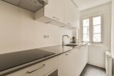 Bu fotoğrafta tezgahların üzerinde beyaz dolaplar ve siyah tezgahlar olan bir mutfak içeriden çekilmiş.