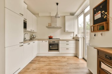 Ahşap döşemeleri ve beyaz dolapları olan bir mutfak duvarda bir fırın.