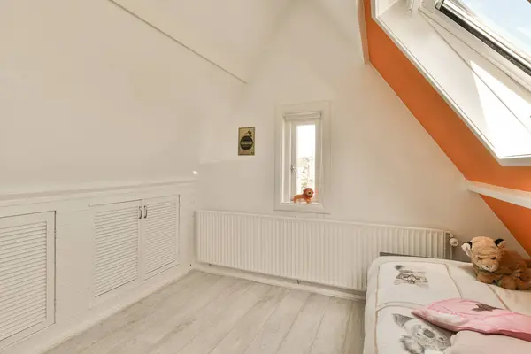 a white room with an orange accent wall and wooden floor in the corner of the room there is a teddy bear on the bed