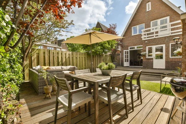 a patio with chairs and an umbrella over the table in front of a large brick house on a sunny day
