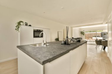 Beyaz dolapları ve siyah granit tezgahı olan modern bir mutfak diğer tarafta açık bir oturma odasında.