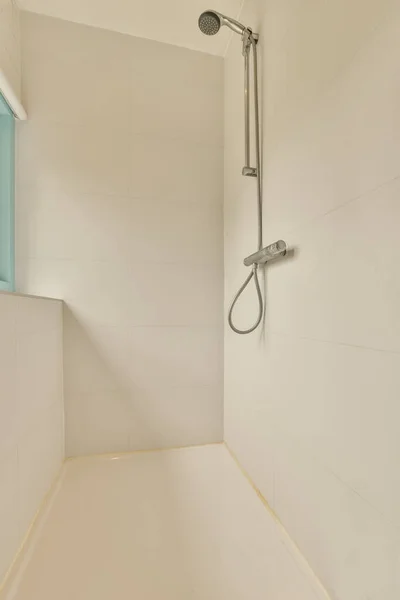 壁に白いタイルが付いている浴室および浴槽の隣に壁に取付けられているシャワーの頭部は青いです — ストック写真