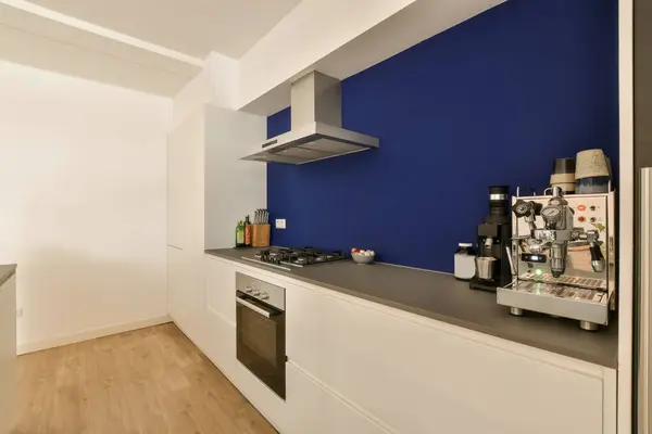 a kitchen area with blue walls and white cupboards on the wall, there is a coffee machine in the corner