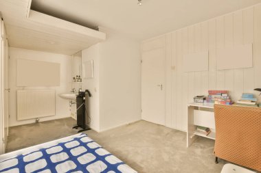 Odanın önündeki duvarda yatağı, masası ve aynası olan bir yatak odası açık bir kapı.