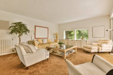 İki koltuklu bir oturma odası, bir sehpa ve resimdeki bir bitki pencereden çekiliyor.