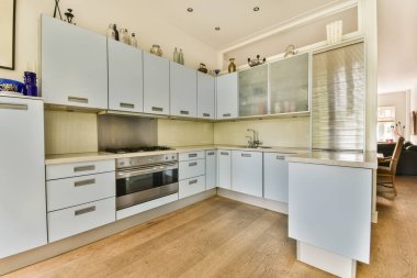 Tezgahın üstünde beyaz dolaplar ve aletler olan bir mutfak. Ahşap döşemeleri olan açık bir alanda.