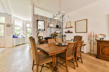 Ahşap döşemeleri ve beyaz duvarları olan bir yemek odası. Odada sandalyelerle çevrili büyük ahşap bir masa var.