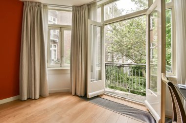 Pencerelerinde kırmızı duvarlar ve beyaz perdeler olan bir oda. Dışarıdaki ahşap zemin olan bir verandaya bakıyor.