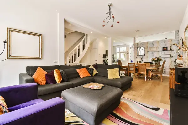 a living room with purple couches and colorful rugs in the center of the room is an open staircase