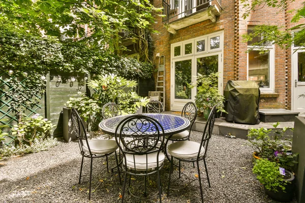 a table and chairs in a backyard area with plants growing on the side of the house to the back door