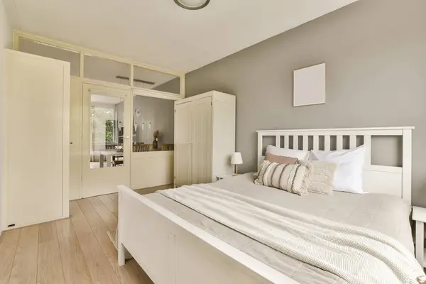 a bedroom with a bed, dressers and mirror in the back wall behind it is a white wardrobe door
