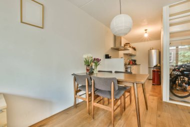 a dining room with wood flooring and white walls, there is an open door leading to the kitchen area