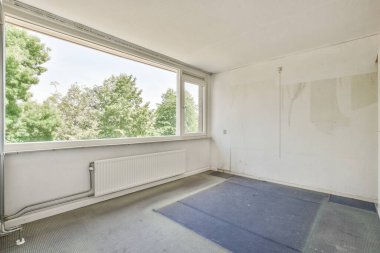 Boş bir oda. Yerde kimse yok. Pencerede ağaçlar görünüyor.