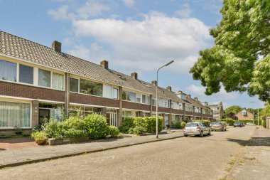 Yan tarafında evler ve arabalar olan bir caddenin önünde yeşil yaprakları olan bir ağaç var.