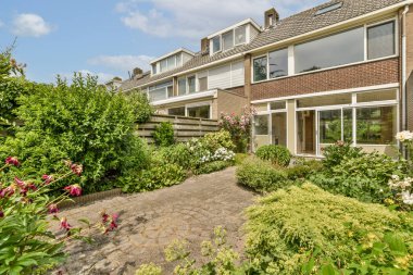 Aydınlık, güneşli bir günde, pencerelerin üzerinde mavi gökyüzü olan bir evin önündeki çiçek ve bitkiler.