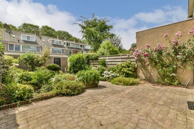 Çiçeklerin ve bitkilerin bulunduğu bir dış alan. Tuğla bir duvarın önünde inşa edilmiş.