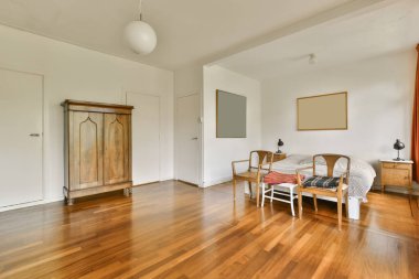 Odasında ahşap döşeme ve beyaz duvarlar olan bir oturma odası nasıl yapıldığını göstermek için dışarı çıkarılır.