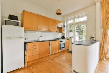 Ahşap döşemeli, ahşap dolaplı ve duvarında beyaz eşyalar olan bir evde mutfak ve yemek odası.