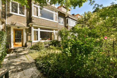 Ön bahçesinde ağaçlar ve çalılar olan bir ev. Arka kapıya giden patikadan görüldüğü gibi.