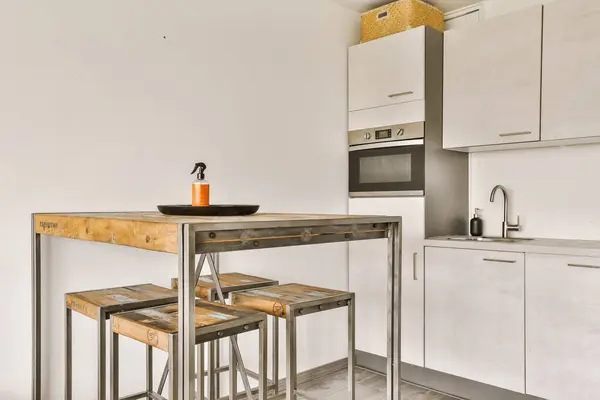 a kitchen area with two stools and a small table in the center of the room, there is a microwave on the wall