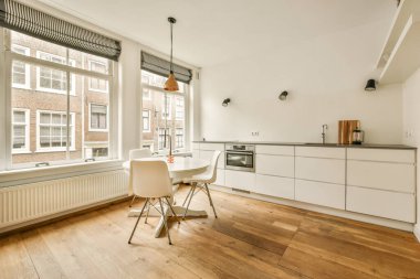 Ahşap döşemeli, beyaz dolaplı ve duvarında fırın olan bir odada mutfak ve yemek odası.