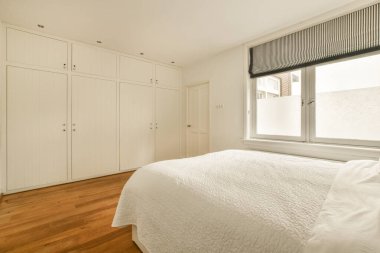 Yatak odası, ahşap döşeme, beyaz dolaplar pencerenin önünde yatağın iki tarafında.