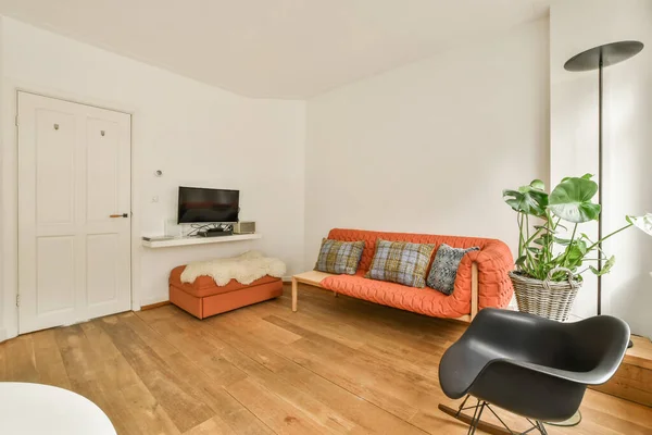 a living room with an orange couch and black chair in front of the sofa is next to a white door