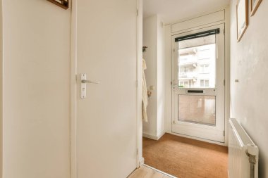 Beyaz duvarları ve kapısında ahşap süslemeleri olan boş bir oda. Köşesinde küçük bir pencere var.