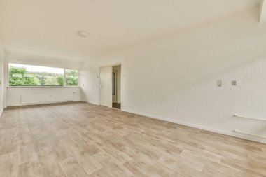 Duvarlarında beyaz boya ve ahşap döşemeleri olan boş bir oturma odası. Köşesinde büyük bir pencere var.